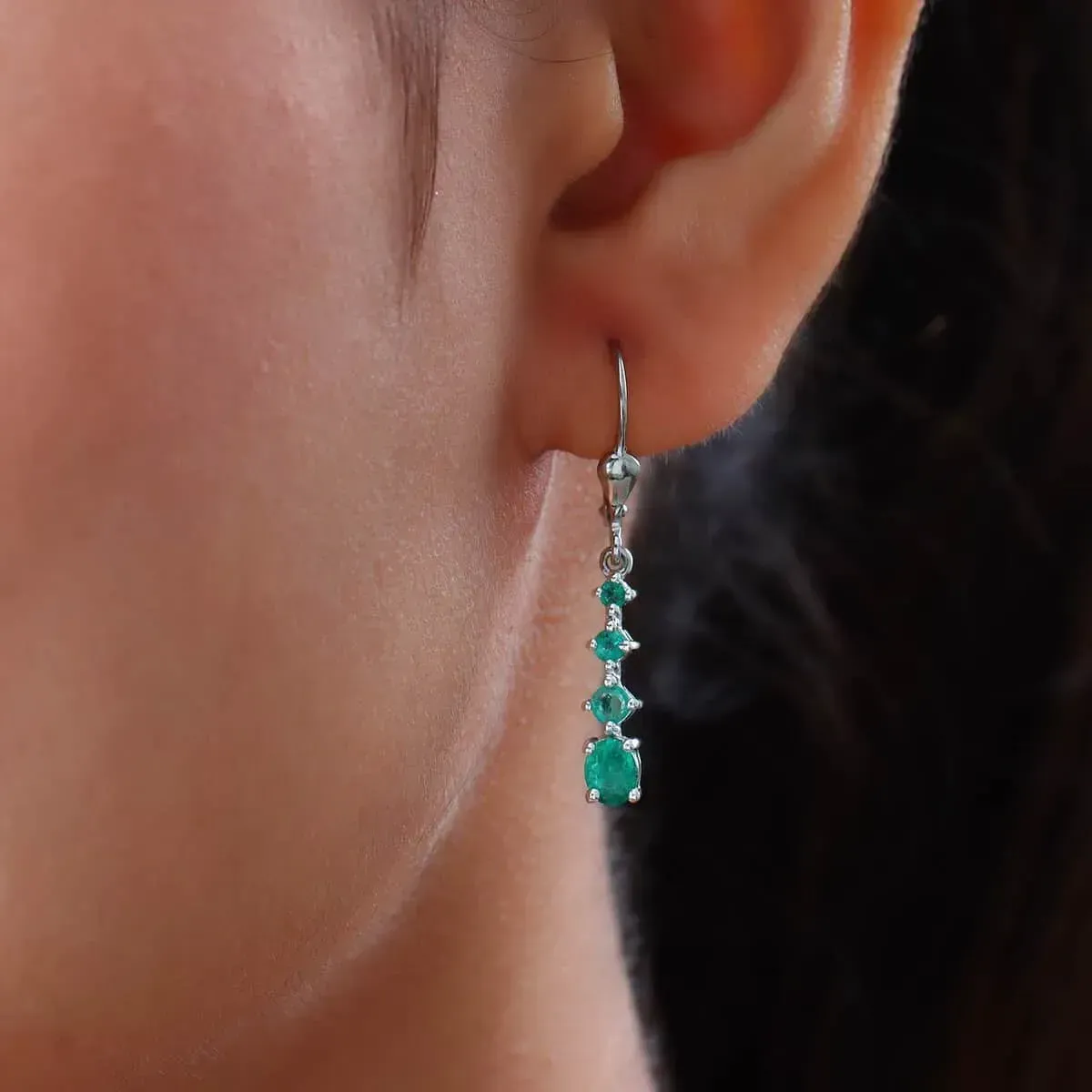 Closeup of woman wearing emerald dangle earrings. 