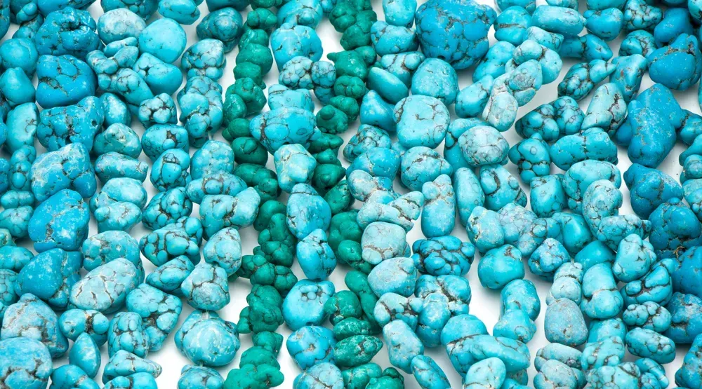 Roughly tumbled turquoise stones on white background.