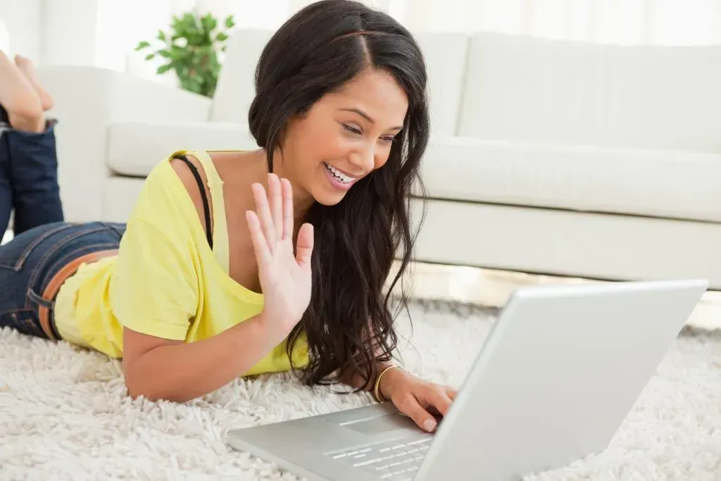 Beaming Latin woman on a video chat while lying on the floor.