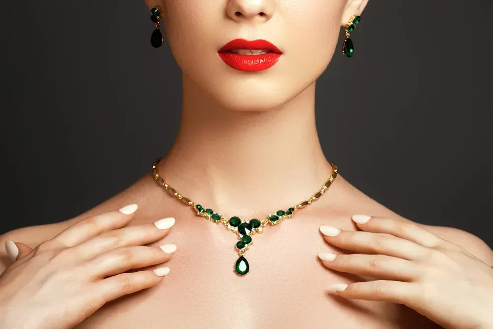 Closeup of woman wearing red lipstick posing with emerald and gold earrings and necklace